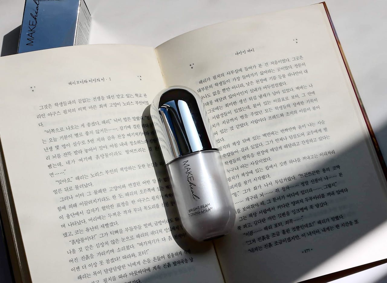 A cosmetic bottle sits on an open book under sunlight, creating a serene atmosphere.